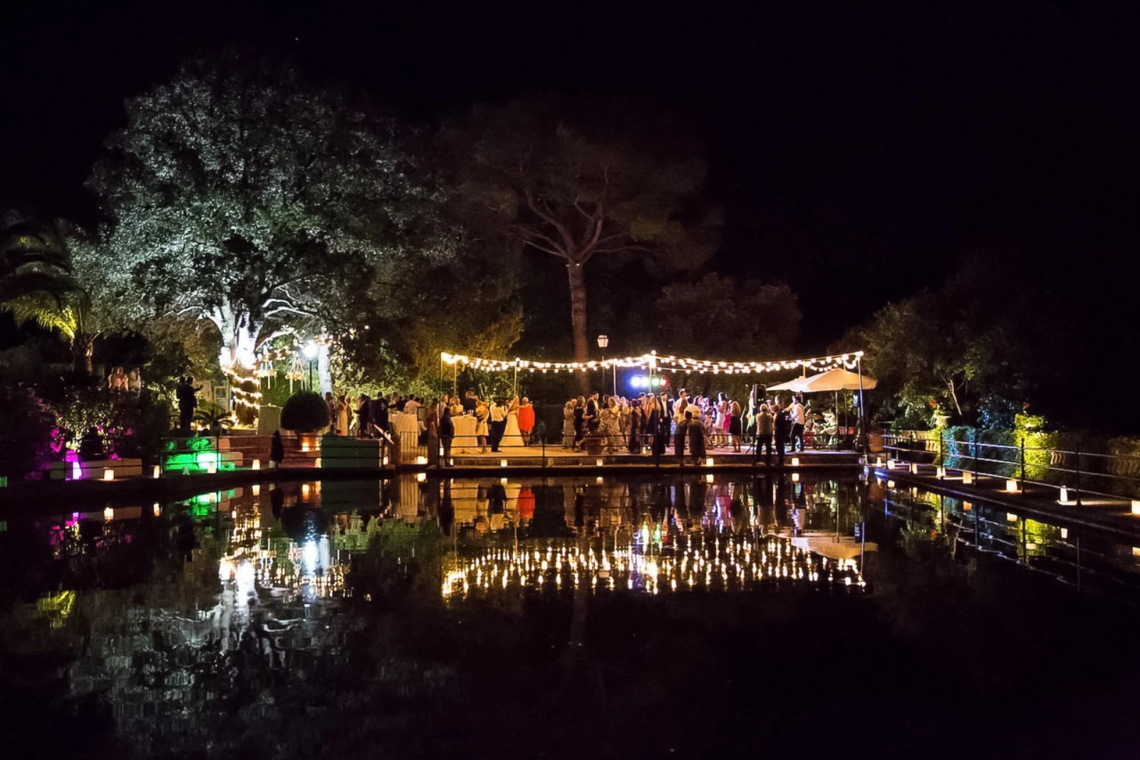 Nächtliche Hochzeitsparty an einem beleuchteten Teich auf Mallorca, Lichter spiegeln sich im Wasser