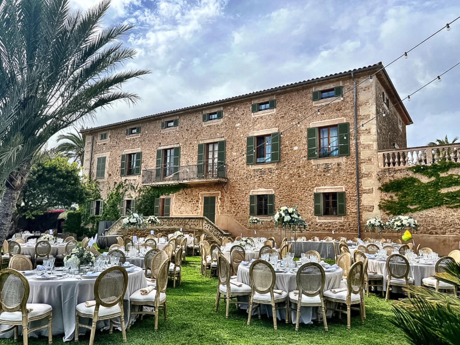 Festlich gedeckte Tische im Garten einer Finca auf Mallorca, mit Palmen und Lichterketten